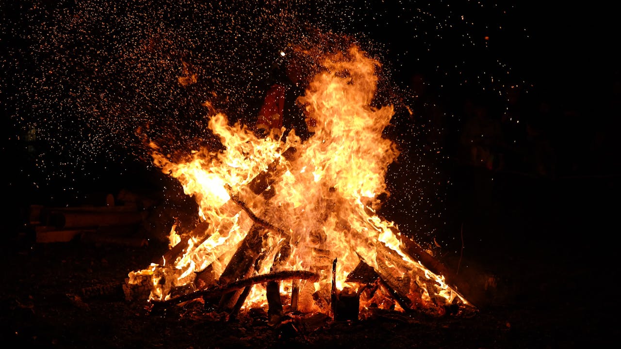 A large bonfire blazing at night with embers and sparks flying into the dark sky.